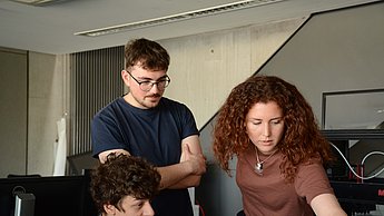 Drei Personen sitzen an Computern