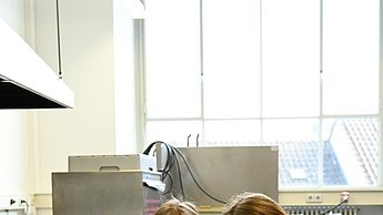Zwei Personen posieren für das Foto. Eine Person hält eine Schüssel mit grünem Inhalt