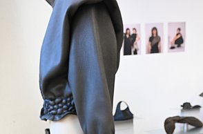 Foto einer Tasche in schwarzen Ledertasche. Dahinter steht ein Oberteil im selben Design