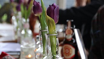 Zwei Tulpen stehen jeweils in Glasflaschen auf einem gedeckten Tisch