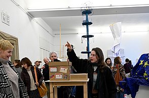 Personen stehen um ein Werk herum während eine Frau ihre Hand über dem Werk hält