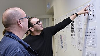 Zwei Männer schauen auf Skizzen auf einer Wand