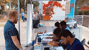 Verschiedene Personen sitzen an einem langen Tisch und zeichnen