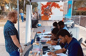 Verschiedene Personen sitzen an einem langen Tisch und zeichnen