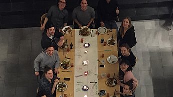 Foto eines langen Tisches an dem viele Personen sitzen und essen 