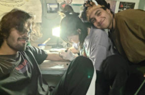 Zwei Personen posieren, während eine dritte im Hintergrund an etwas arbeitet