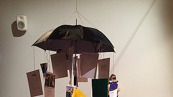Foto einer ausgestellten Werks, dass aus einem Regenschirm, Luftballons und Polaroidfotos besteht