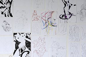 Verschiedene Skizzen sind nebeneinander aufgehängt. Es sind abstrakte Menschen zuerkennen