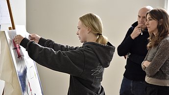 Frau klebt Papier an Staffelei 