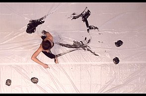 Eine Person verbreitet schwarze Farbe auf einer großen Leinwand