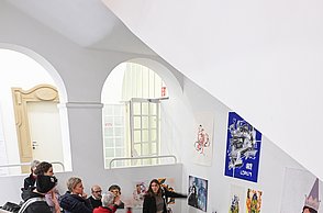 Personen laufen eine Treppe herab während sie die vielen Bilder an den Wänden betrachten