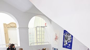 Personen laufen eine Treppe herab während sie die vielen Bilder an den Wänden betrachten