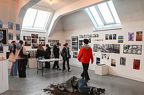 Foto einer Ausstellung bei welcher Bilder an den Wänden hängen und eine Skulptur auf einem Häufchen Erde auf dem Boden liegt