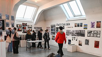 Foto einer Ausstellung bei welcher Bilder an den Wänden hängen und eine Skulptur auf einem Häufchen Erde auf dem Boden liegt
