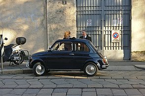 Foto eines kleinen, dunkelblauen Autos, dass vor einem Tor geparkt ist