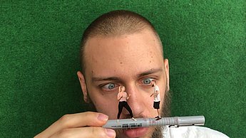 Bild eines Mannes, der zwei winzige Menschen auf einem Fineliner balancieren sieht