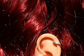 Foto eines Ohrs mit Ohrringen in glänzendem, roten Haar